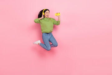 Full size photo of cute young lady jump listen music wear pullover jeans footwear isolated on pink background