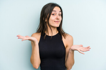 Young caucasian woman isolated on blue background doubting and shrugging shoulders in questioning...
