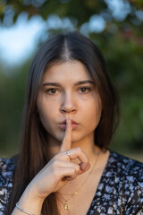 Fototapeta na wymiar Portrait of beautiful young girl with long hair holding a finger to her lips with a face expressing fear or ordering silence, Poland
