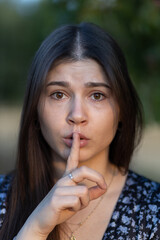 Fototapeta na wymiar Portrait of beautiful young girl with long hair holding a finger to her lips with a face expressing fear or ordering silence, Poland