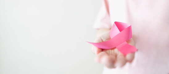 Breast Cancer Awareness Month in October. Close up of woman in pink shirt holding satin pink ribbon...