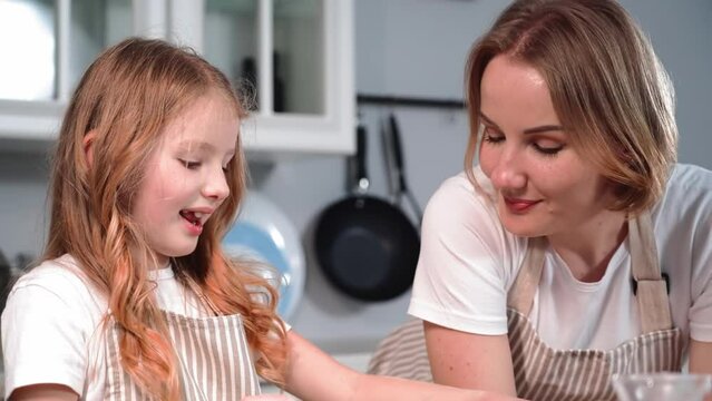 motherhood, loving mother together with her cute daughter preparing cookies from dough talking and gently touching nose to nose in background of kitchen