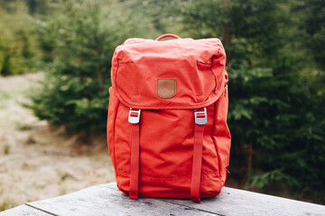 Hipster red backpack. View from front tourist traveler bag with forest background. Travel outdoor...