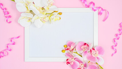 Romantic copy space framew ith orchid flowers and ribbons on pastel pink background. Flat lay