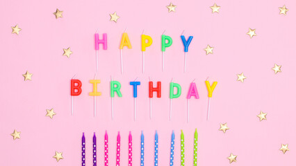 Happy birthday text with candles and stars on pastel pink background. Flat lay