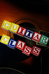Word or phrase Guitar Class made with letter cubes, standing on guitar.