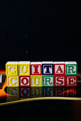 Word or phrase Guitar Course made with letter cubes, standing on guitar.