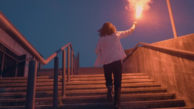 Teenager running up stairs with burning signal flare in raised hand, slow motion back view. Teen protest, rebellion demonstration, resistance, leadership concept