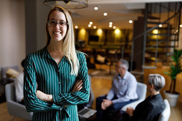 Portrait of a confident casual businesswoman in office smiling while colleagues are having a meeting in background