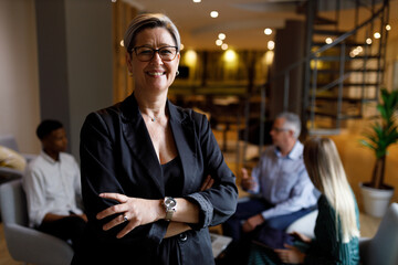 Portrait of a confident casual businesswoman in office smiling while colleagues are having a meeting in background