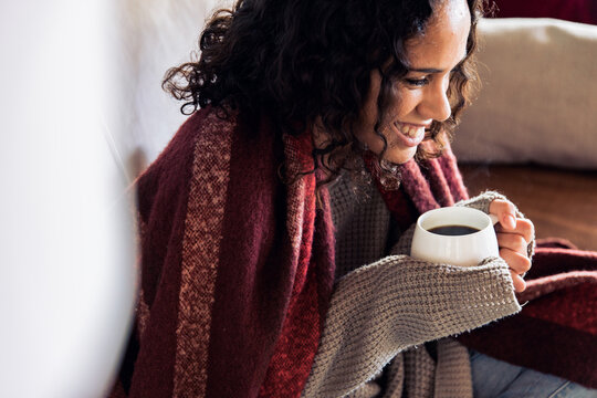 Young hygge woman drinking warm coffee on sofa at home