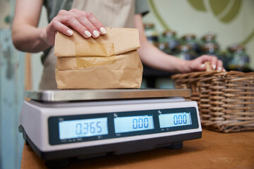 Close Up Of Sales Assistant In Sustainable Plastic Free Grocery Store Weighing Goods In Paper Bag...