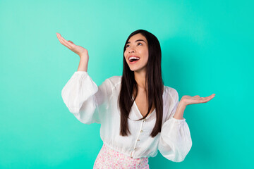 Photo of positive pretty girl raise arms palms catch look empty space isolated on vivid aquamarine...