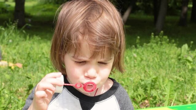 A little white girl blows soap bubbles. A sunny summer day in the park.