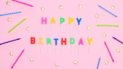 Happy birthday text with candles and stars on pastel pink background. Flat lay