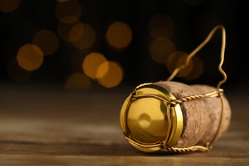 Closeup view of sparkling wine cork and muselet cap on wooden table against blurred festive lights,...