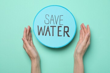 Woman holding hands near card with words Save Water on turquoise background, top view