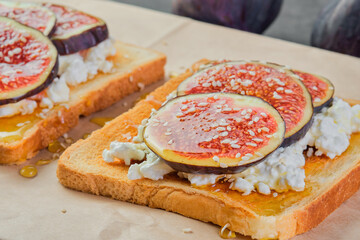Bruschetta with figs honey, sesame seeds and fresh soft cheese, on craft paper backing, close-up, selective focus on toast