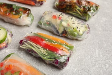 Many different delicious rolls wrapped in rice paper on grey table, closeup