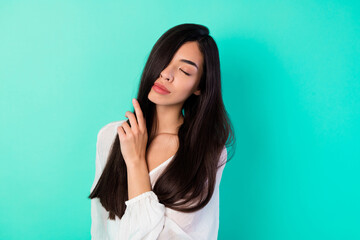 Fototapeta premium Portrait of tender pretty thai girl closed eyes hand touch black hair isolated on vivid cyan color background