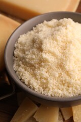 Delicious grated parmesan cheese in bowl on wooden table, closeup