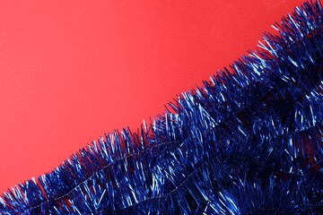 Bright blue tinsel on red background, top view. Space for text