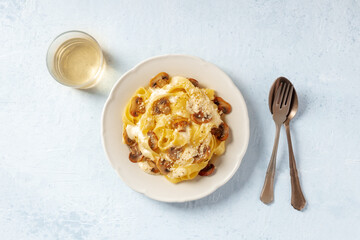 Pappardelle pasta with mushrooms, cream sauce and cheese, overhead flat lay shot with a glass of white wine