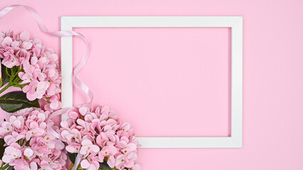 Copy space white frame with romantic pink flowers on pastel pink background. Flat lay