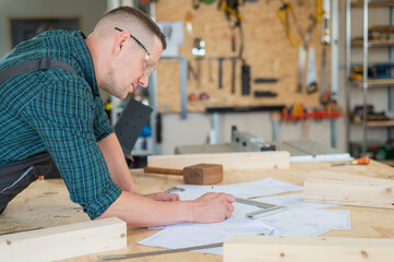 A portrait of a carpenter in goggles and work overalls draws a blueprint for a workshop.