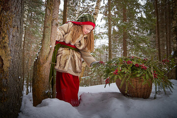 Little girl in old peasant clothes including a fur coat and a shawl in a cold winter forest with...