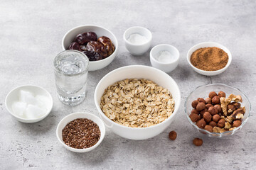 Ingredients for cooking healthy oatmeal cookies: oatmeal, flaxseed, nuts (hazelnuts and walnuts), coconut oil, water, dates, coconut sugar, salt and baking powder on gray textured background