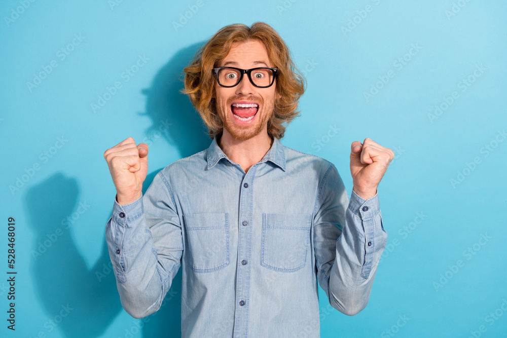 Poster Portrait of delighted overjoyed man raise fists celebrate triumph accomplishment isolated on blue color background