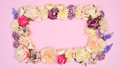 Copy space frame made with natural spring flowers on pastel pink background. Flat lay