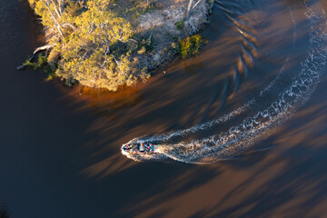 Aerial view of a boat speeding round a hairpin bend in a murky river lined with gumtrees