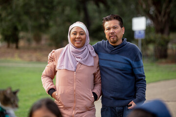 Smiling middle aged woman wearing pink hijab and a middle aged woman putting his arm around her