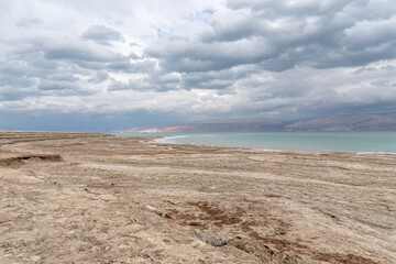 Exotic view of the sinkhole area of the Dead Sea on a stormy winter day. PhotoStorm and rain at the Dead Sea coastline. Salt crystals at sunset. The texture of the Dead sea. Salty seashore. High