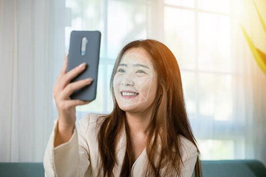 Asian women use smartphone for access control face recognition in private identification on sofa living room at home, Asian female checking her personal data scanning face by mobile phone to unlock