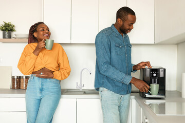 Happy african american couple preparing fresh aromatic coffee with machine in kitchen, enjoying hot...