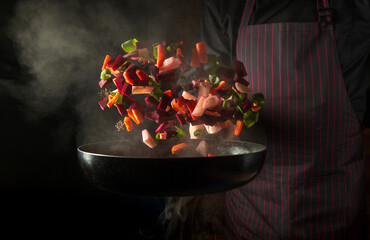 Chef prepares food in a hot pan with steam on a black background. The concept of restaurant and hotel service. Grande cuisine.