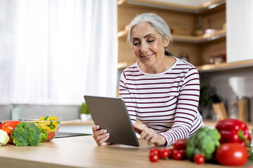 Portrait Of Happy Senior Woman Using Digital Tablet While Cooking In Kitchen