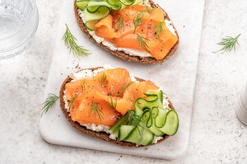 Rye bread open sandwiches with salted salmon and cucumber on a white stone table. Healthy food.