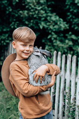 A cute boy is holding a rabbit and looking at the camera. outdoor