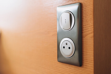 Gray plastic walk-through switch and socket on a wooden wall. Closeup view