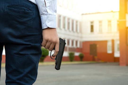 Firearms At School. A Teenager With A Gun On The Background Of The School. A Man Goes To School With A Gun. School Violence