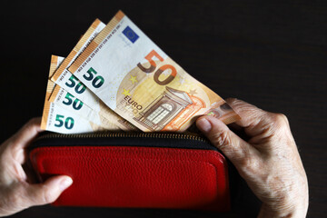 Euro banknotes in wrinkled hands, elderly woman takes out money from red wallet. Concept of pension payments and assistance, savings, retirement in Europe