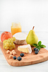 Blurred image of grapes, nuts, camembert, pear, peach, blueberry and honey on a light table.