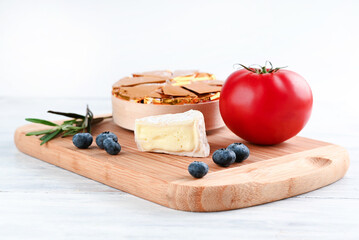 Camembert, blueberry, tomato, rosemary sprig on a wooden board on a light table.