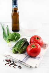 Blurred image of tomato and cucumbers on a towel, basil and onion, olive oil on a light table.