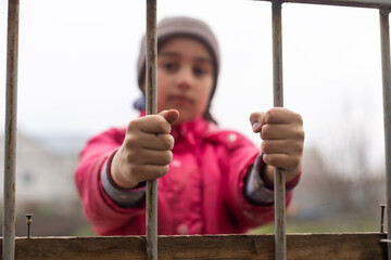 Little girl behind bars. Concept of homeless children. Child captivity. Sad child