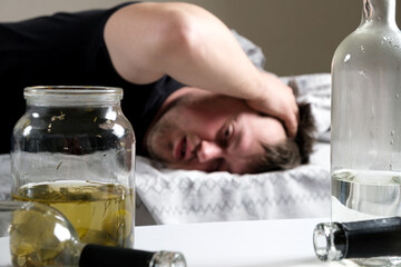A drunk man lies in bed, holding his hands to his head. Hangover, alcoholic delirium.